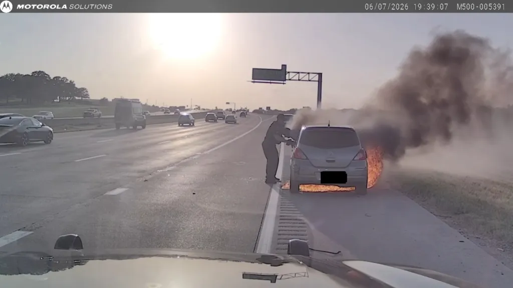 A person extinguishing a car fire on the side of a highway.