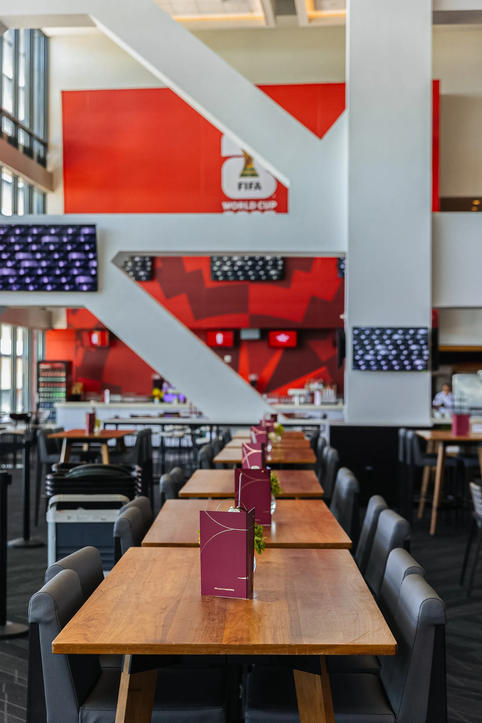 Interior of a FIFA World Cup suite with long wooden tables and grey chairs.