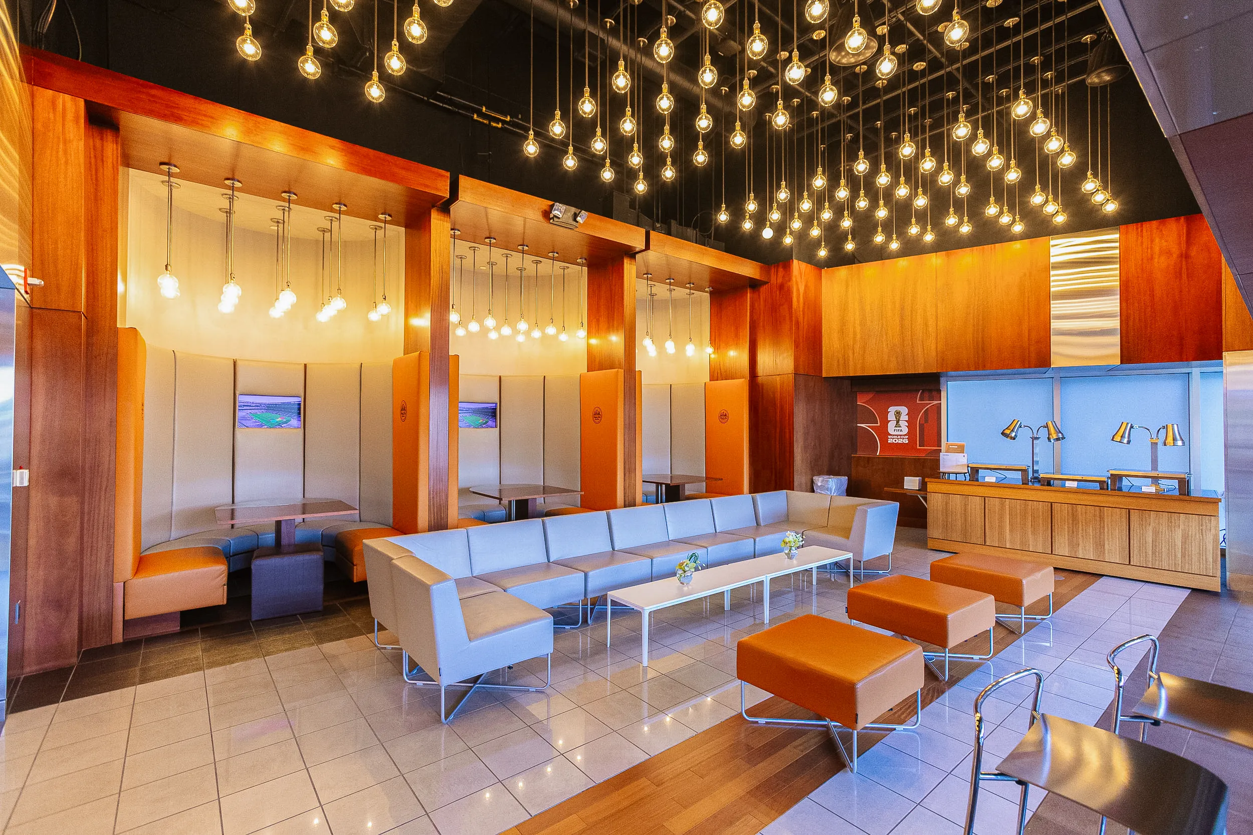 The interior of the FIFA suites 2026 lounge features various seating arrangements and a buffet station, all illuminated by numerous hanging lightbulbs.
