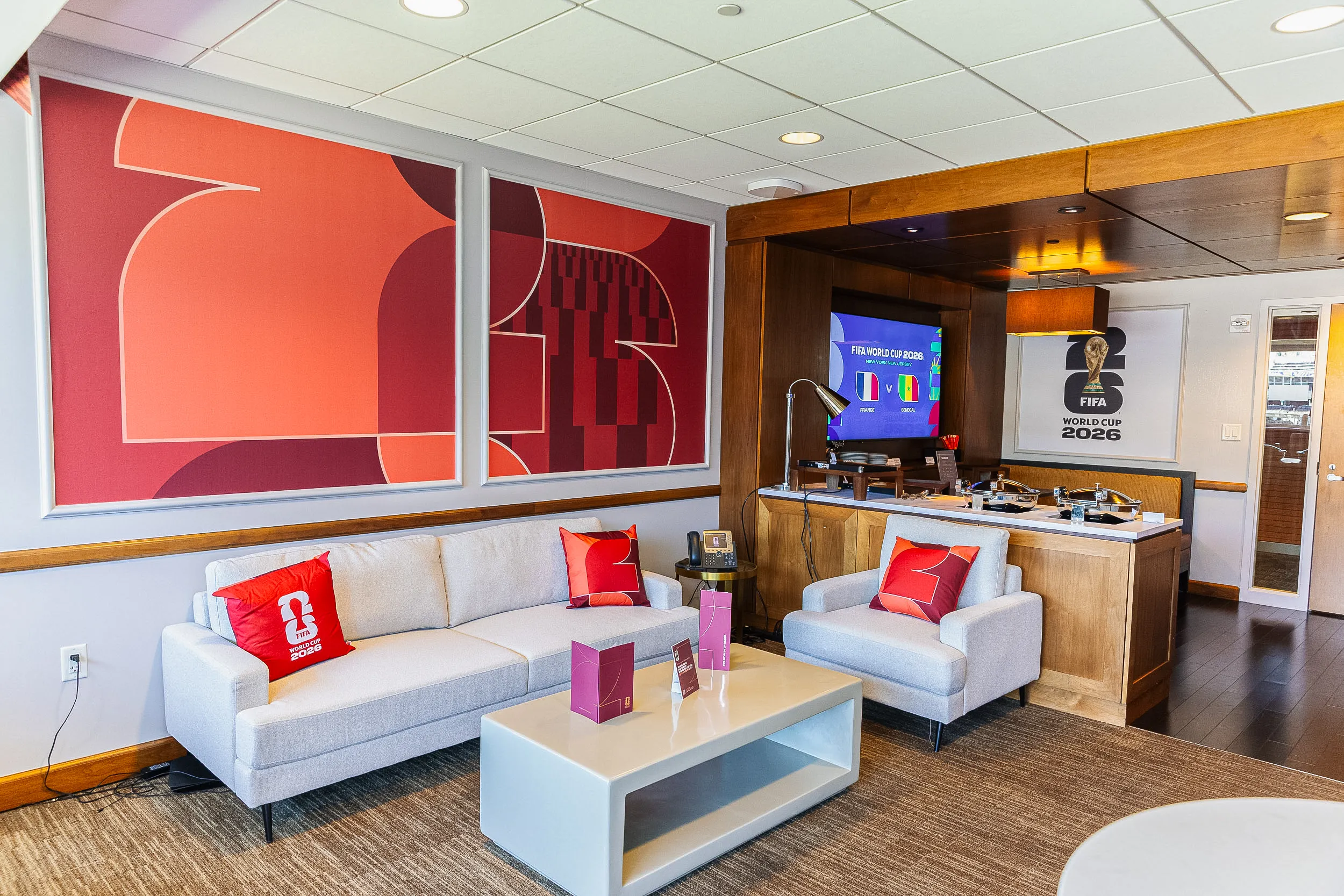 A living room-style FIFA World Cup 2026 suite with a sofa, armchairs, coffee table, and a large TV displaying 