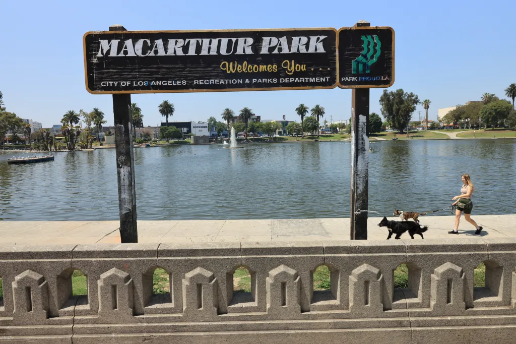 A welcome sign for MacArthur Park in Los Angeles, California, with a lake and palm trees in the background.