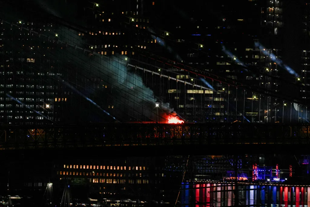 A fire caused by fireworks burns on the Brooklyn Bridge, with smoke billowing from the structure, as the US celebrates its 250th anniversary on Independence Day.