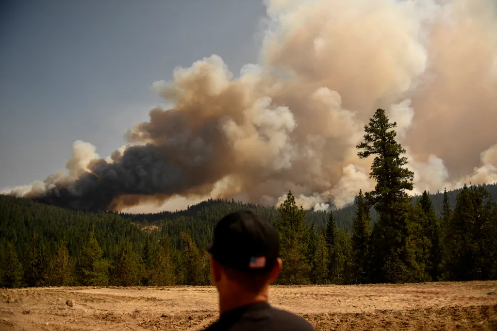 A firefighter looks from Fredonyer Pass as smoke plumes from spot fires rise during the Dixie Fire.
