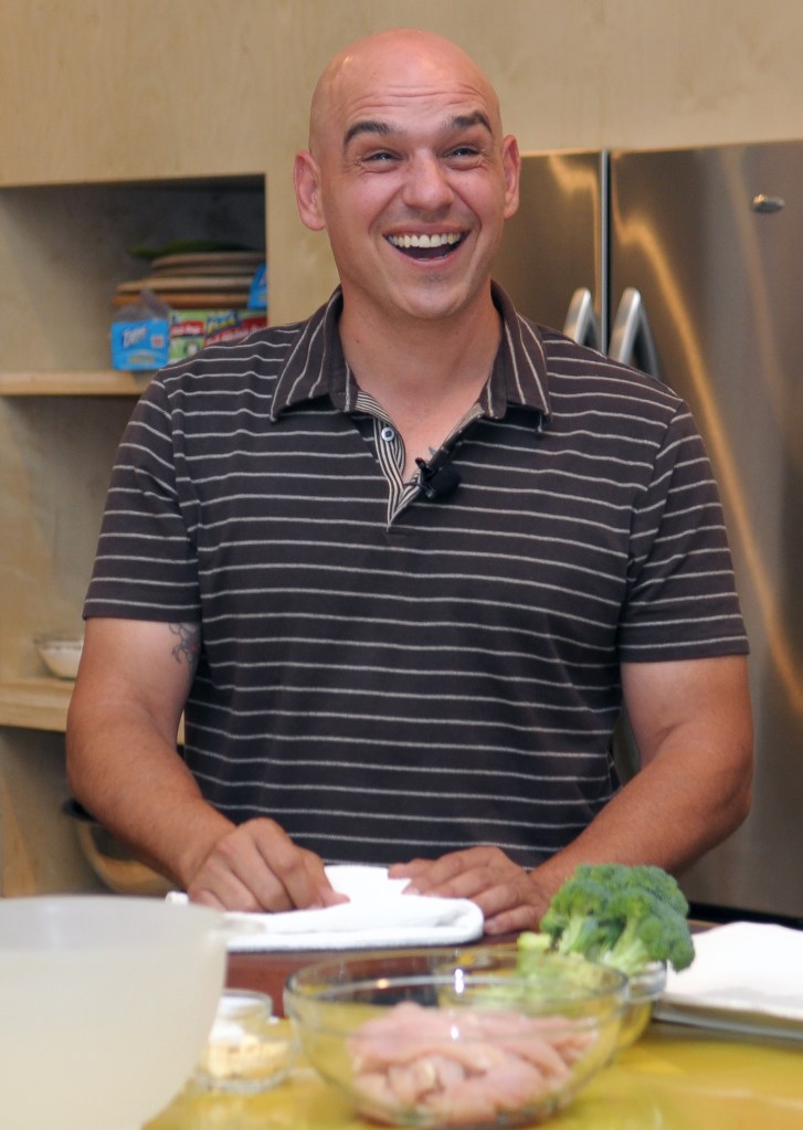 Chef Michael Symon laughing during a cooking demonstration.