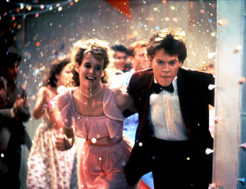 Lori Singer and Kevin Bacon running through confetti, dressed in formal attire.