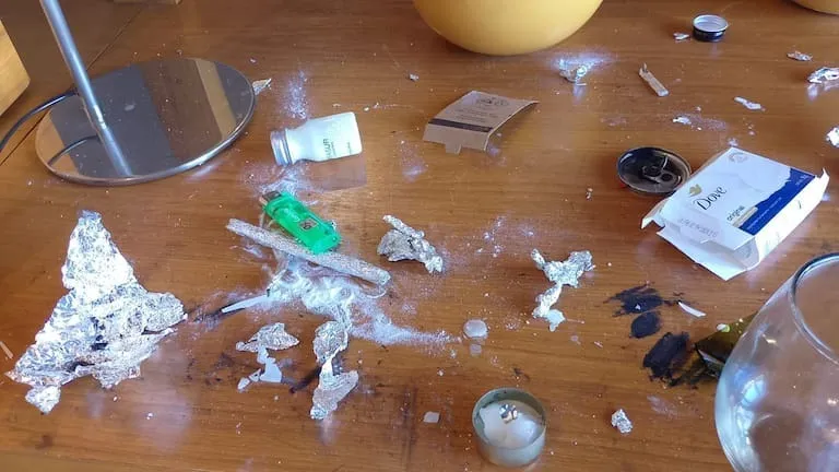 Hotel room table covered with drug paraphernalia, including tinfoil, a white powder, a lighter, a small bottle, and a can.