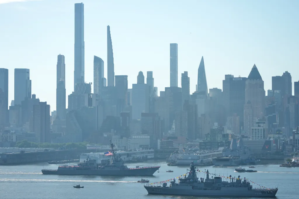 The USS Farragut and another military ship decorated with flags sail in the Hudson River with the New York City skyline in the background.