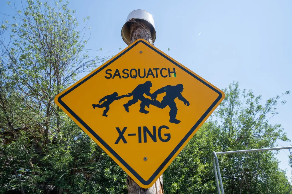 Funny yellow sign with a black border, showing three Sasquatch figures running, and the words 