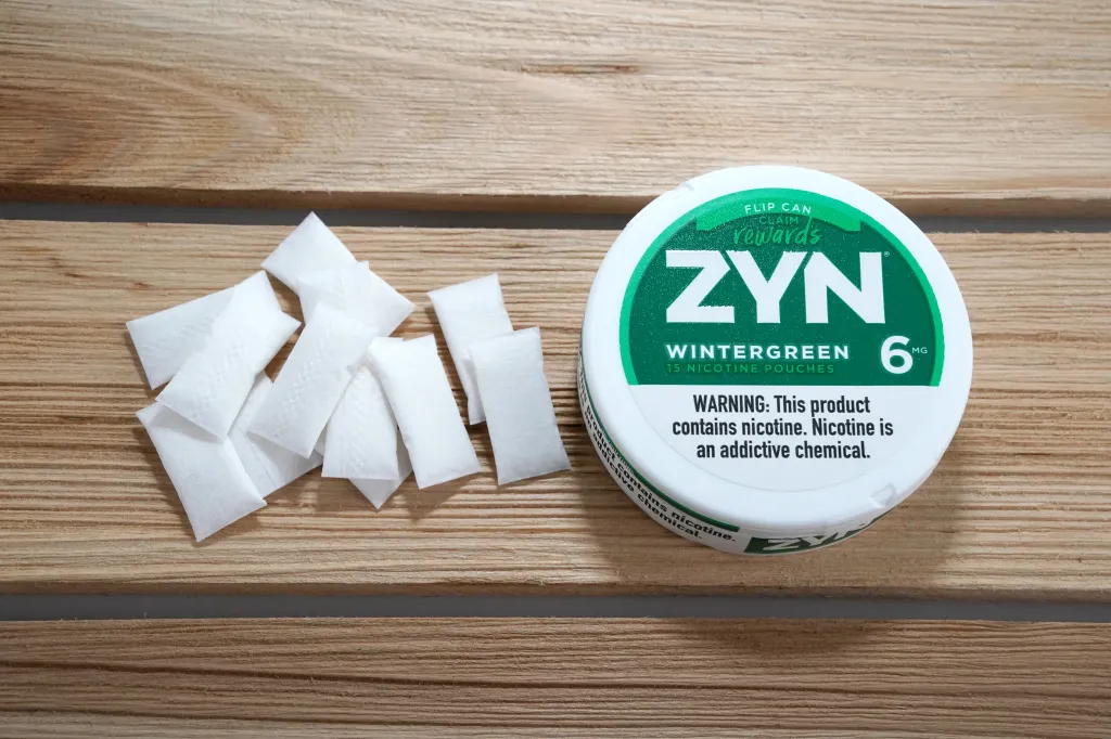 A package of Zyn Wintergreen nicotine pouches next to several white nicotine pouches on a wooden surface.