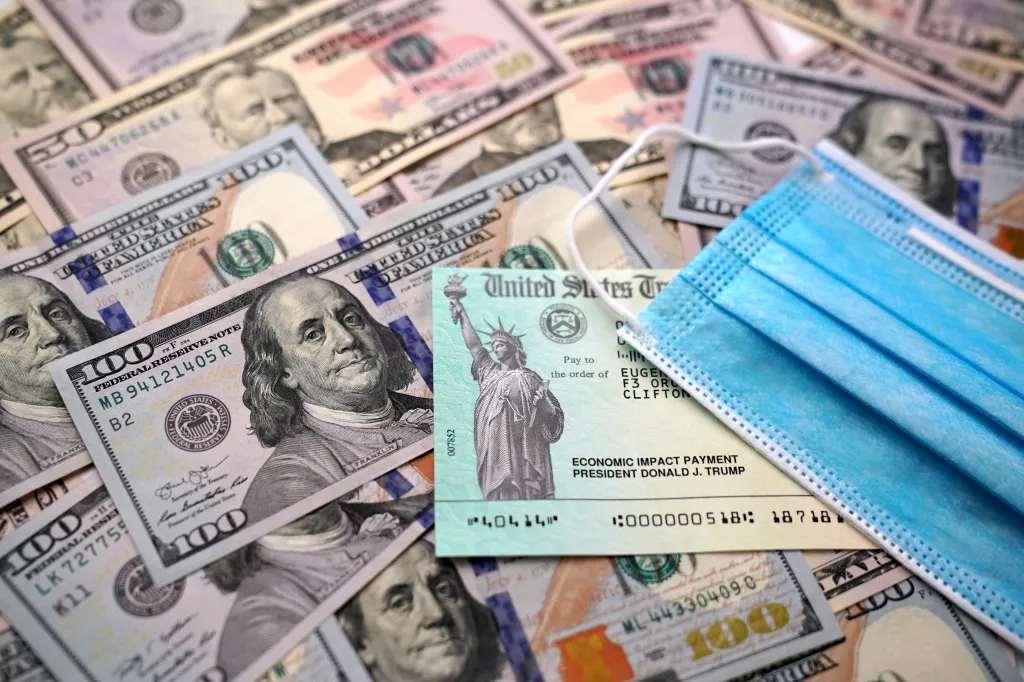 A CARES Act stimulus check, US currency, and a face mask.