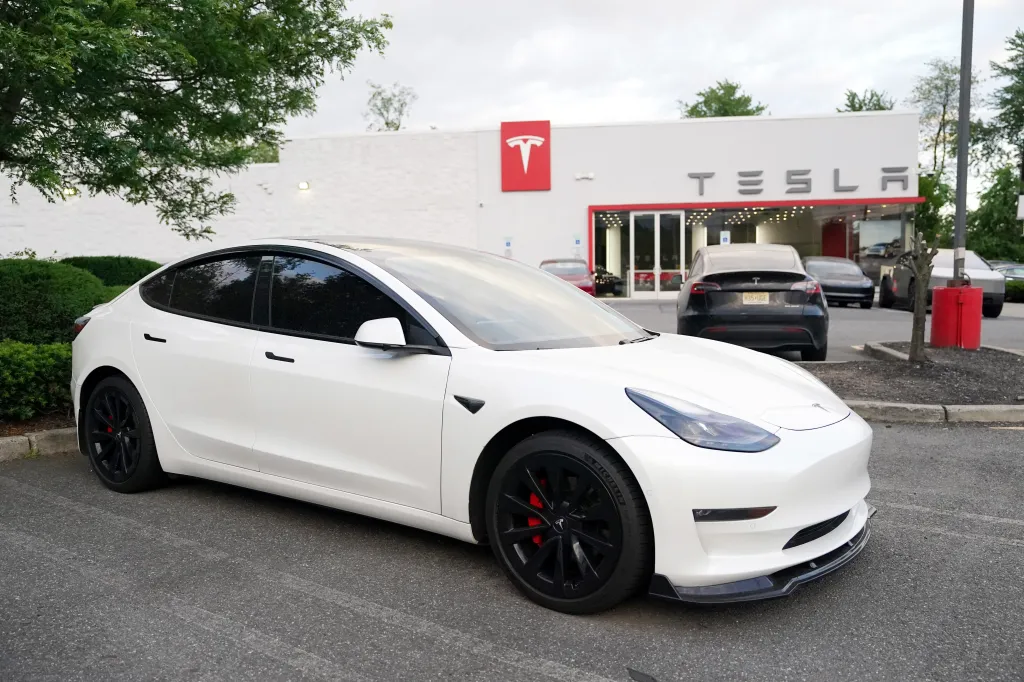 A white Tesla car parked in front of a Tesla dealership building.