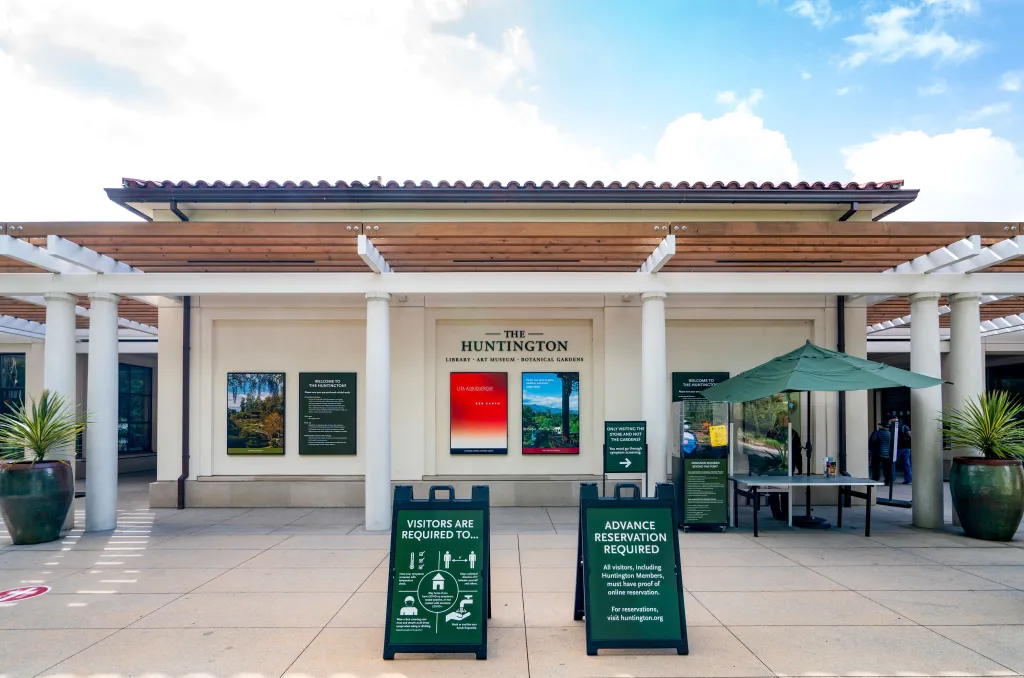 The entrance to The Huntington Library, Art Museum, and Botanical Gardens, with signs detailing visitor requirements for health and reservations.
