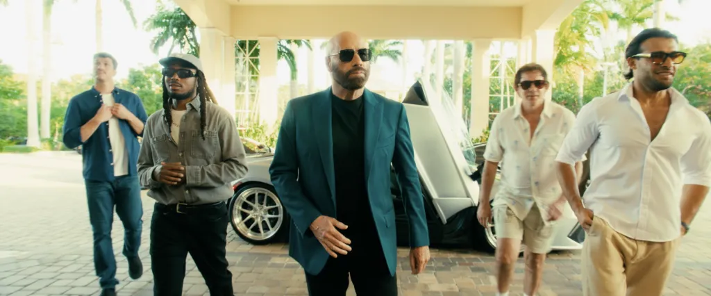 John Travolta, in a blue jacket, black T-shirt and black pants and sunglasses, and Sam Asghari, far right, in a white shirt and beige pants and sunglasses, with other cast members in