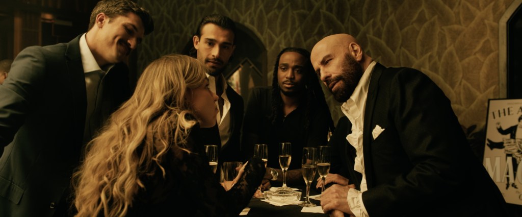 John Travolta , in a black suit and wtie shirt, and Sam Asghari in a scene from