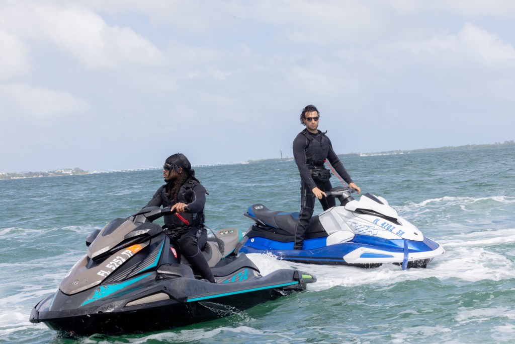Sam Asghari, in a black wetsuit, and a co-star on jet skis in