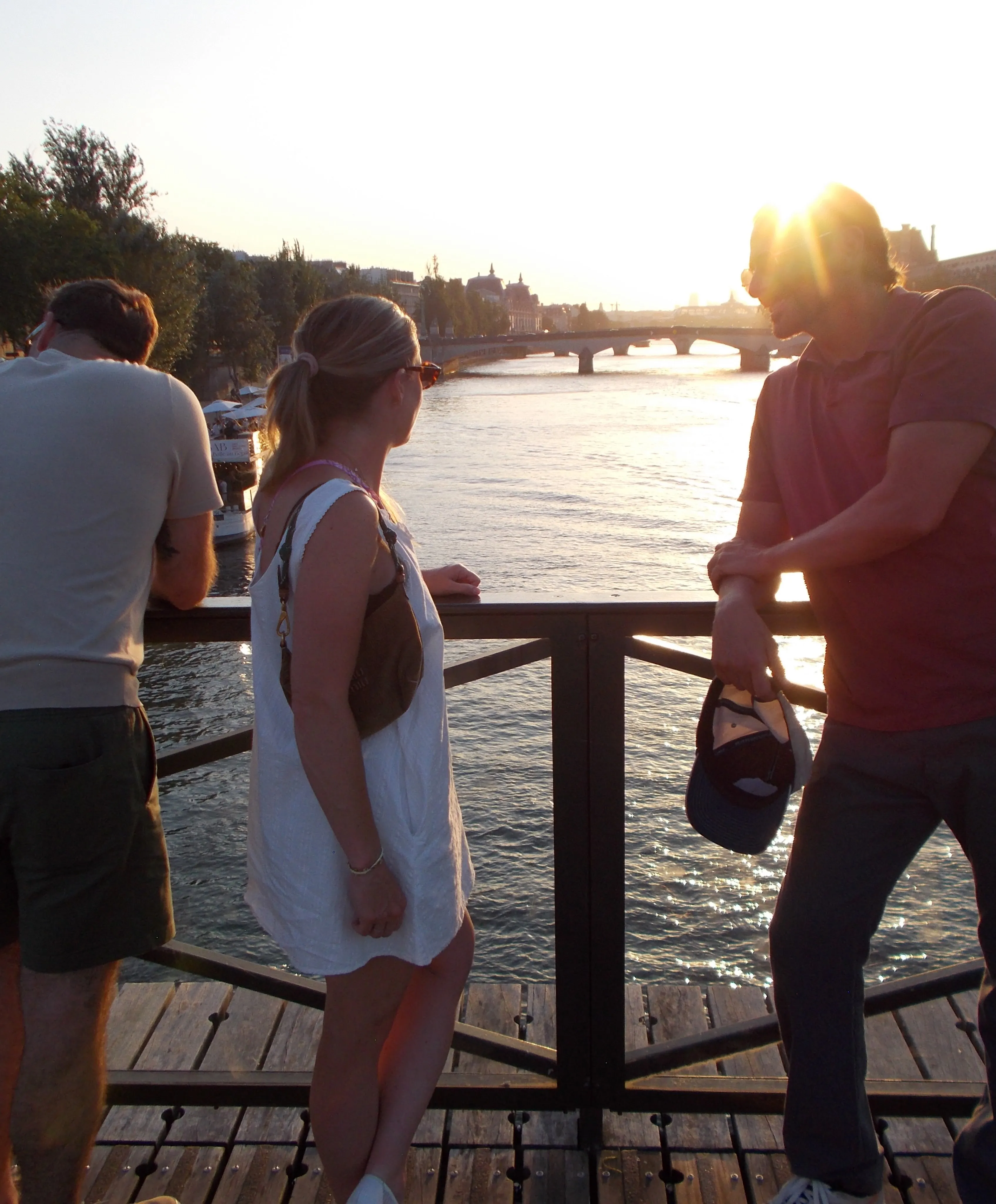 Three people on Pont des Arts bridge in Paris at sunset.