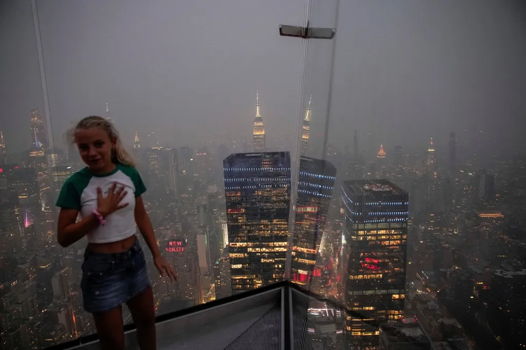 A girl reacts as the New York City skyline and the Empire State Building are seen from the Edge observation deck through a cover of wildfire smoke in New York City, U.S., July 16, 2026.