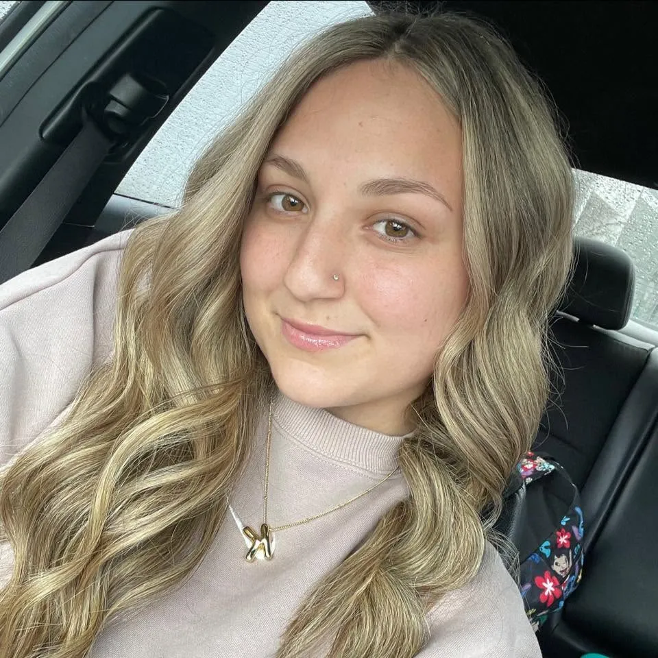 Katie McCormack, a young woman with long blonde hair, smiles at the camera while seated in a car.