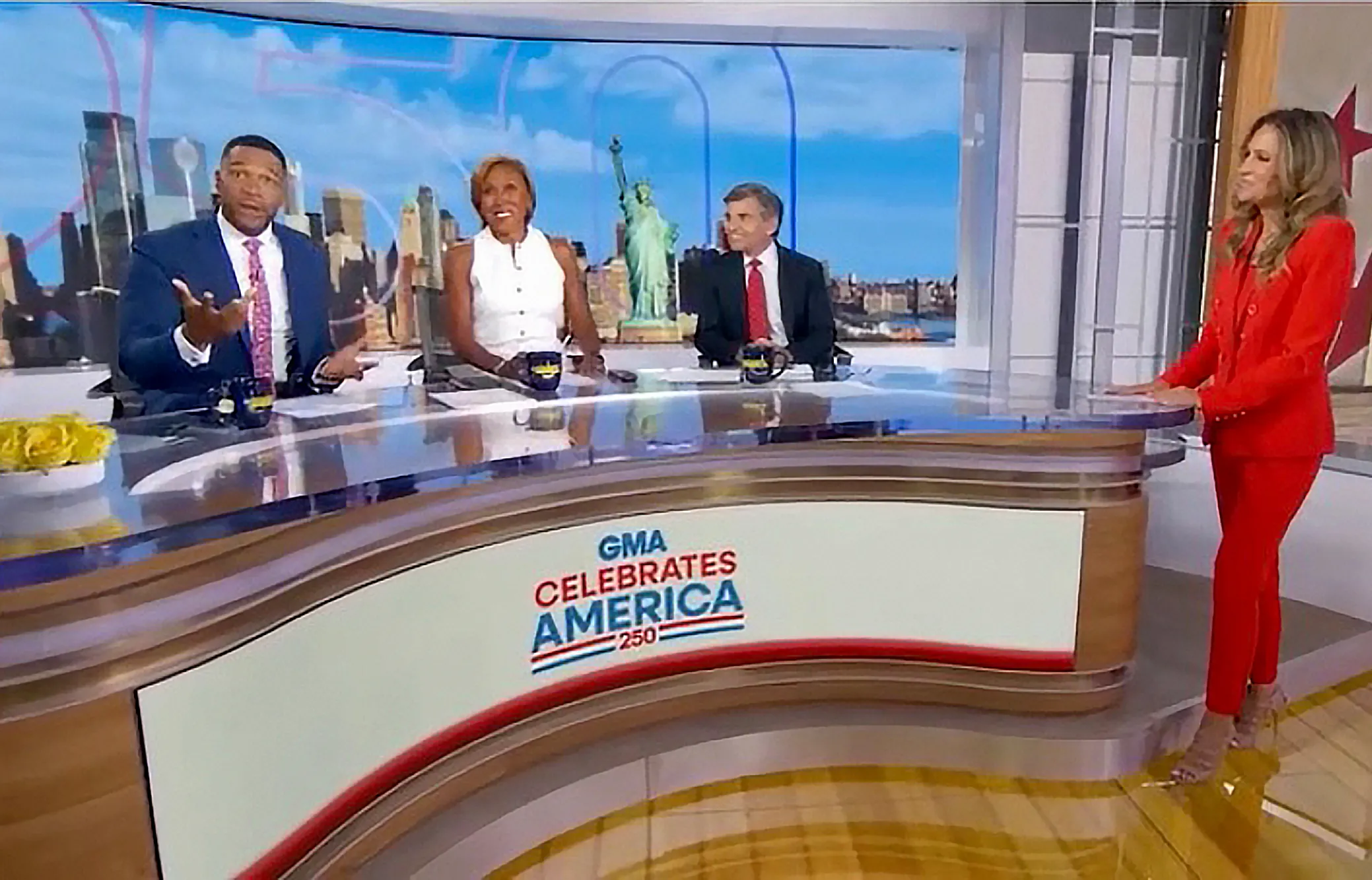 Good Morning America co-hosts Robin Roberts, Michael Strahan, George Stephanopoulos, and an unknown woman in red, discussing an 