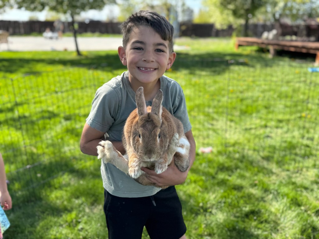 A smiling Graham Summers holding a large brown rabbit in his arms outdoors.