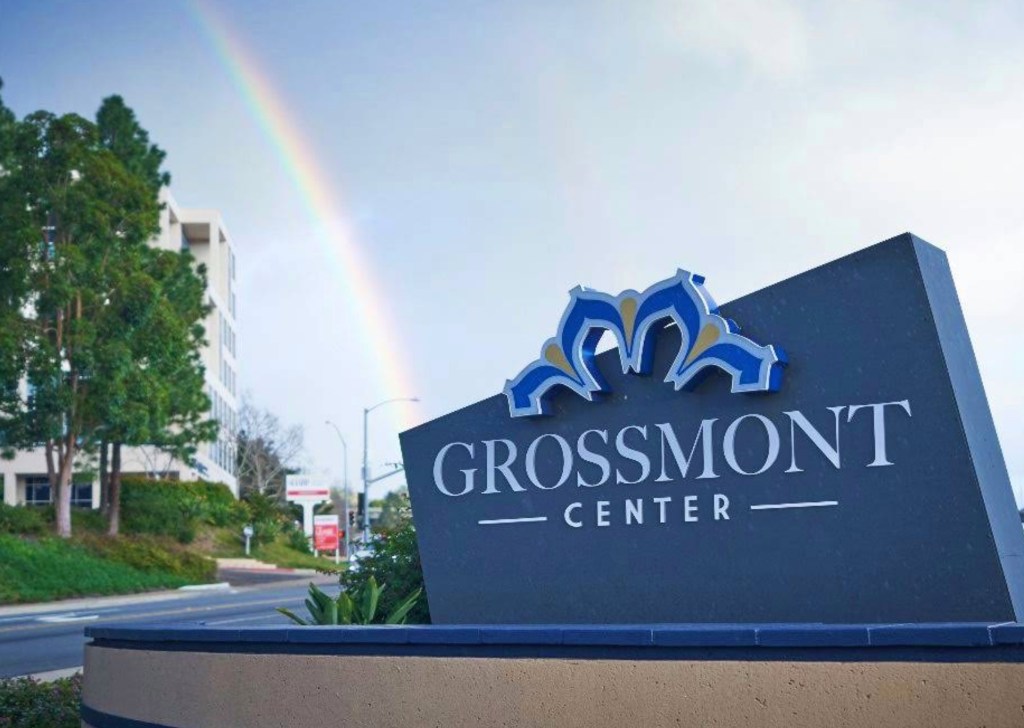 A rainbow over the Grossmont Center sign, with a building and trees in the background.