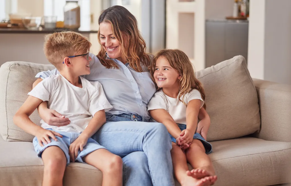 A smiling mother sitting on a couch with her son and daughter, both smiling.