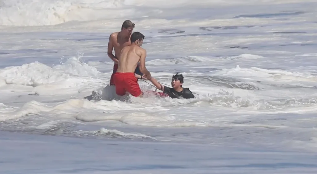 Two lifeguards rescue a young boy from rough waves at the beach.