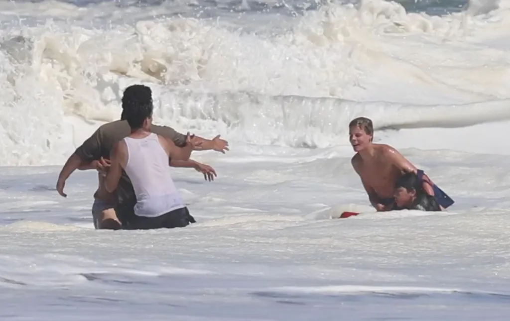A young lifeguard rescuing a boy from a large wave.