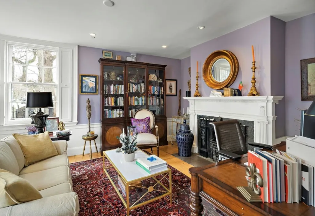 Living room of the Lindall-Gibbs-Osgood House with purple walls, a white couch, a fireplace, and a bookshelf.
