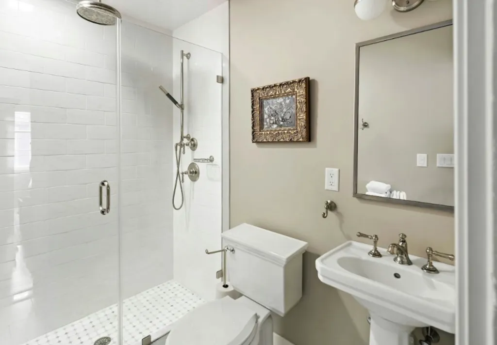 Bathroom with a white tiled shower, toilet, and sink.