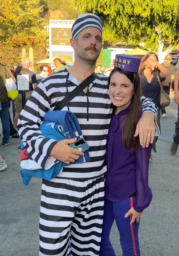 A man in a prisoner costume with his arm around a woman in a purple top and 
