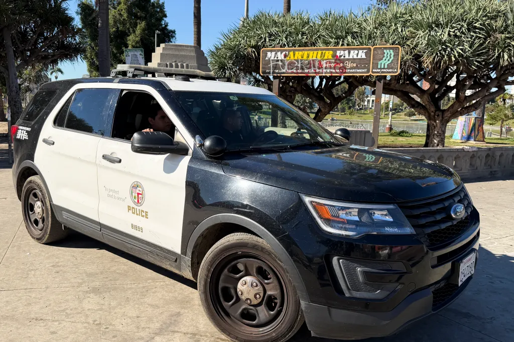 Black and white police SUV parked in front of a MacArthur Park sign.