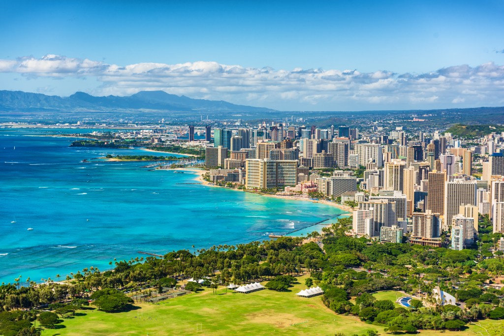 Aerial view of Honolulu and Waikiki Beach from Diamond Head, showing the city skyline, coastline, and blue ocean.