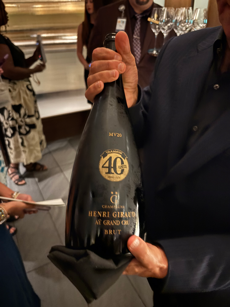A person holds a large bottle of Henri Giraud Ay Grand Cru Brut champagne with a Yaamava' 40th-anniversary logo.