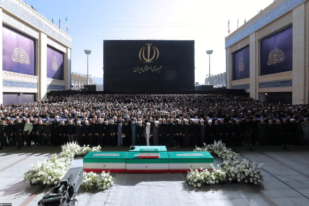 A large crowd attends a public farewell ceremony for Iran's late Supreme Leader at the Imam Khomeini Grand Mosalla, with three caskets draped in the Iranian flag in the foreground.