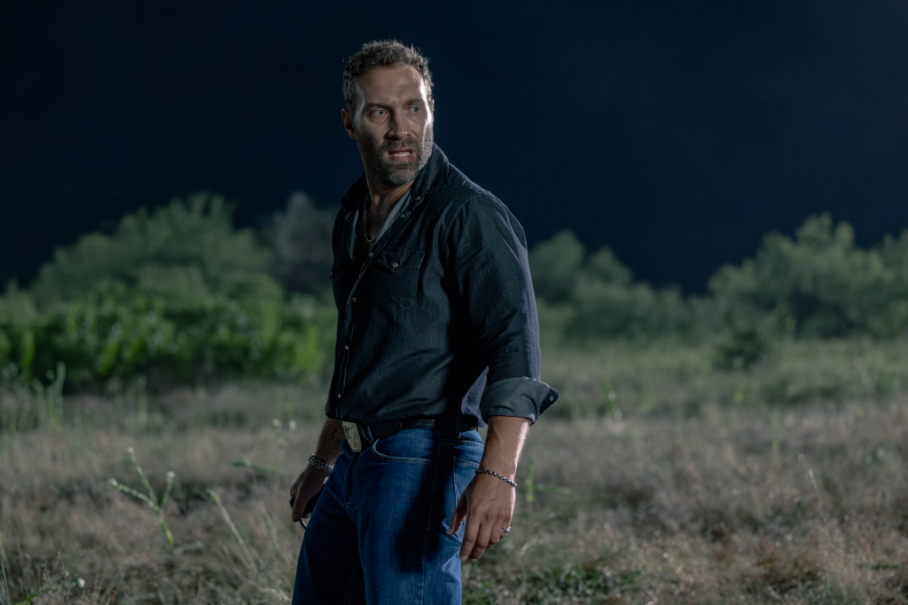 Rob-Will Jackson, portrayed by Jai Courtney, wearing a dark shirt and jeans, looks nervously over his shoulder at night.