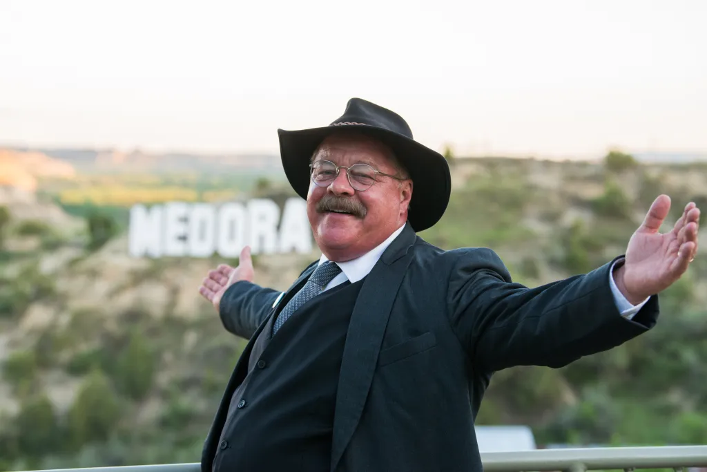 Joe Wiegand as Teddy Roosevelt with his arms outstretched in front of a 