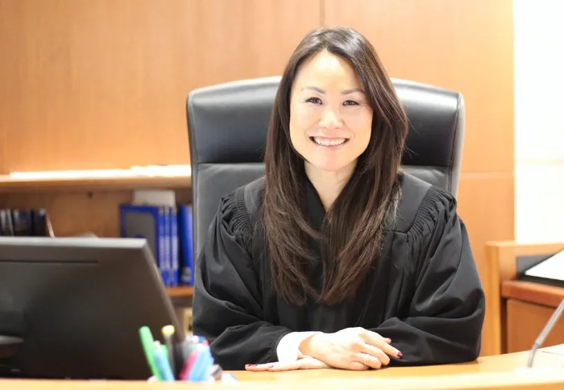 Judge Lana Kim smiling in her judicial robes at a desk.