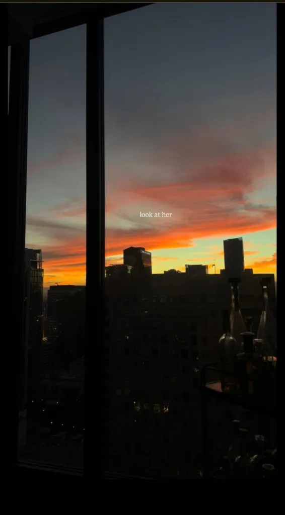 View of a vibrant sunset over a city skyline from a window, with the text 