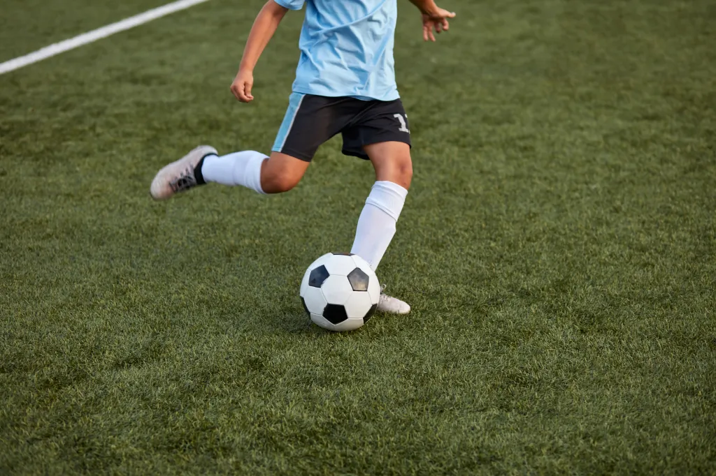 Boy in a blue uniform and black shorts kicking a soccer ball on a green field.