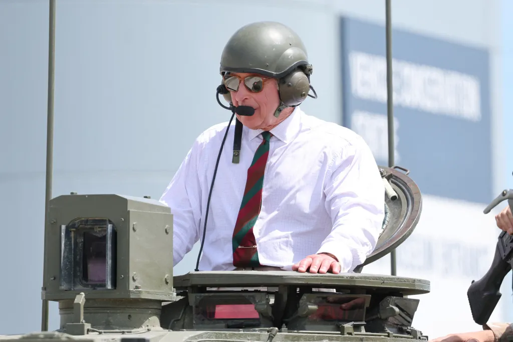 King Charles III, in a white shirt and a red striped tie, wearing a helmet and headset in a Challenger 3 tank.