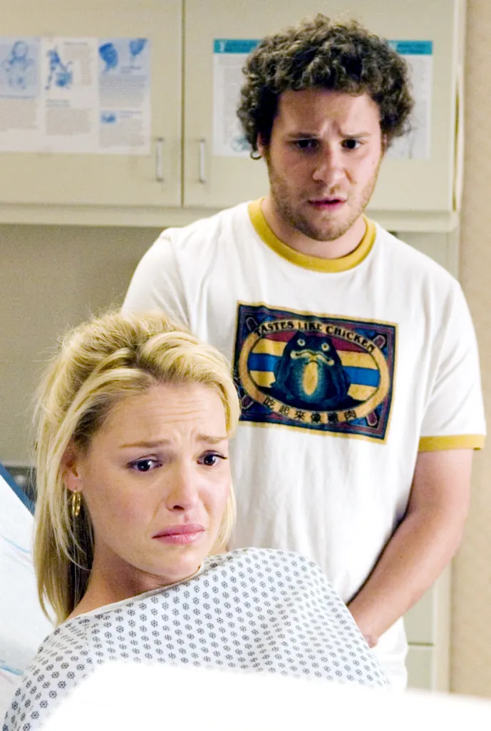 Katherine Heigl, wearing a hospital gown, crying in the foreground with Seth Rogen, looking nervous, behind her.