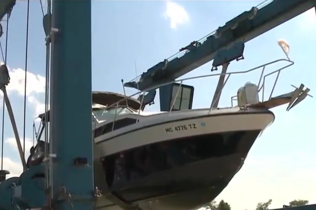 A boat being lifted from the water by a large blue crane, with 