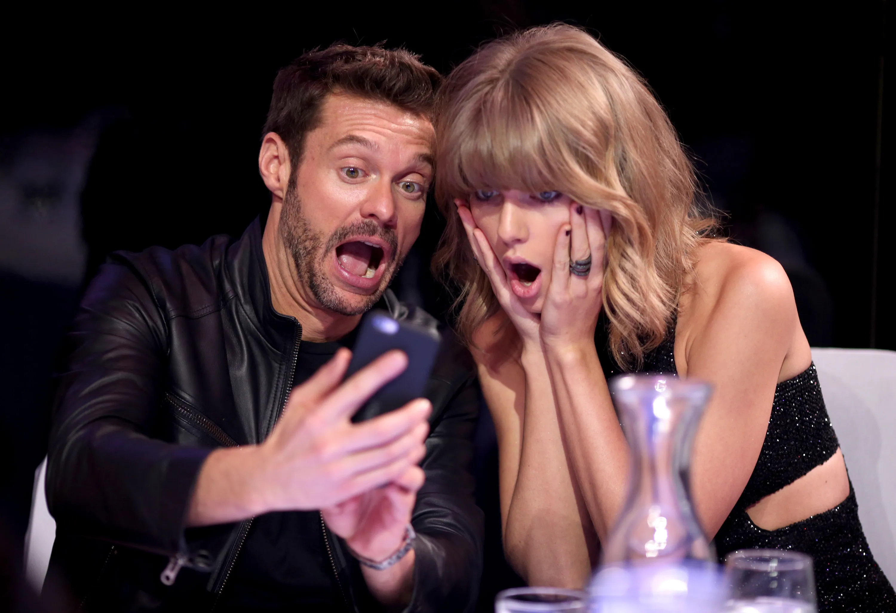 Ryan Seacrest taking a selfie with Taylor Swift, both making surprised faces.