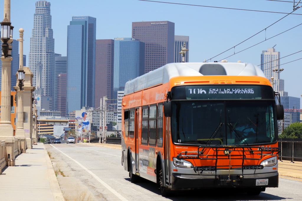 A Los Angeles Metro bus on a bridge with downtown LA skyscrapers in the background.
