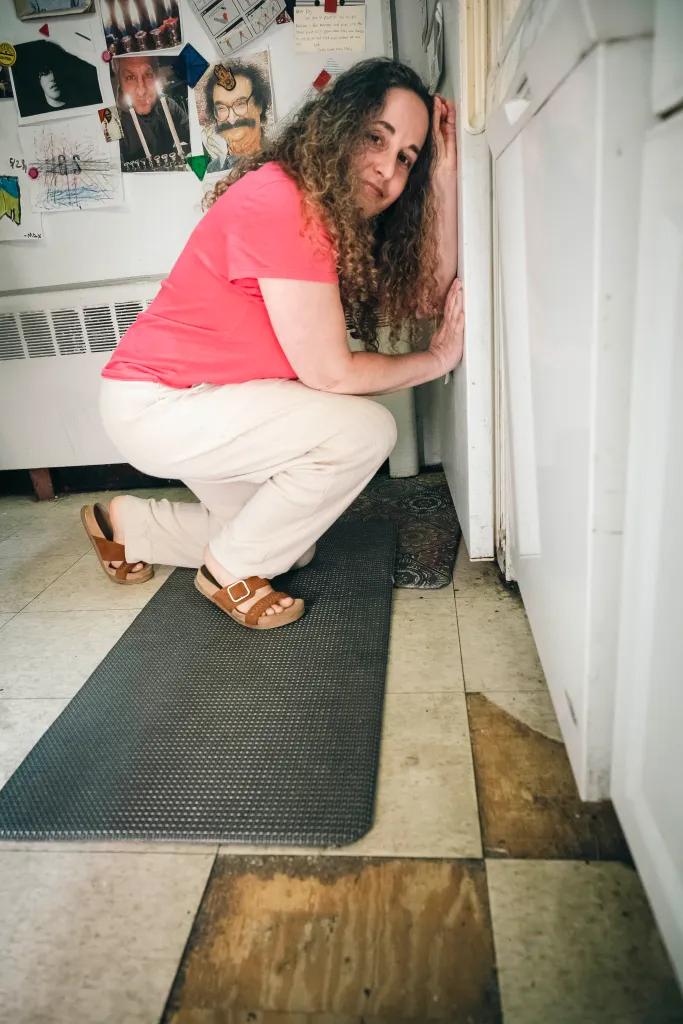 Lara Kossover in a pink shirt and tan pants bends down on a black mat.