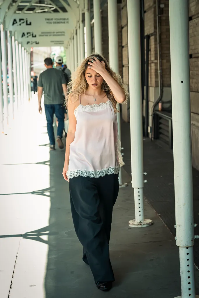 Lauren Holaday in a light pink lace-trimmed camisole and black pants walks under an awning in Nolita.