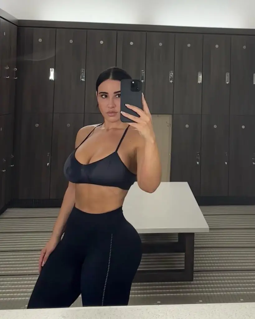 Lauren Pisciotta, in a black sports bra and leggings, taking a mirror selfie in a locker room.