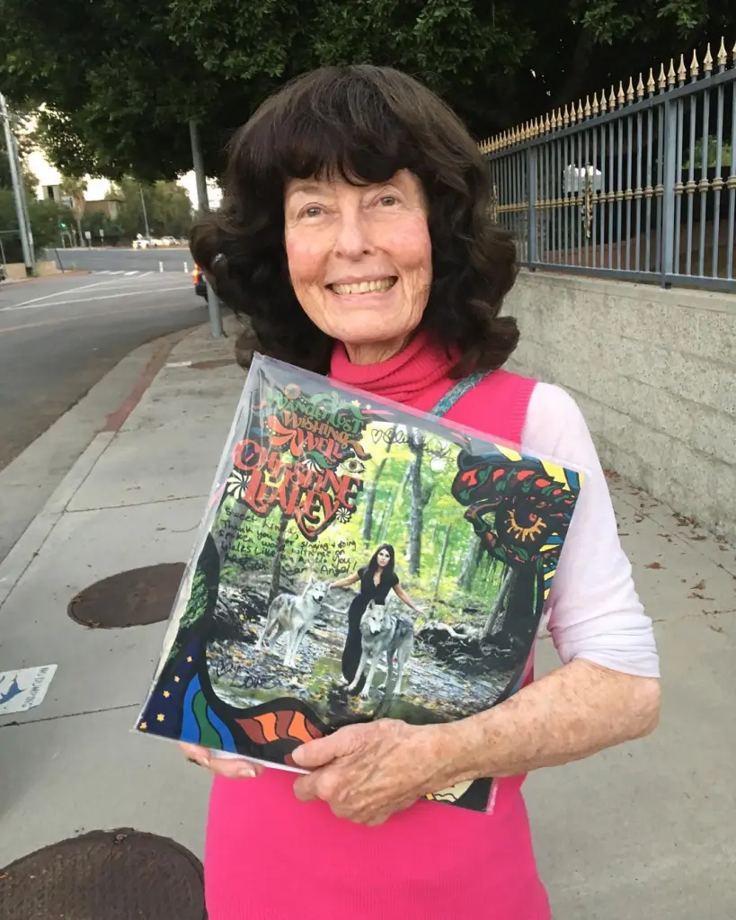 Linda Perhacs holds up a signed album on a sidewalk.