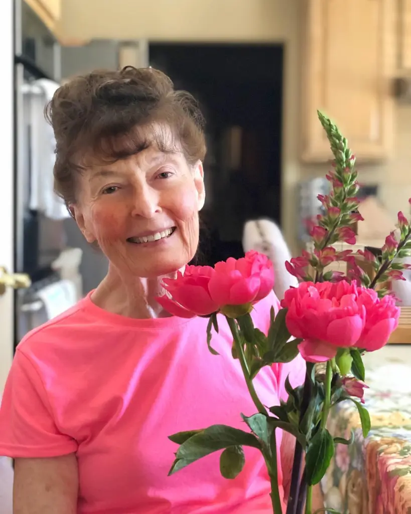 Linda Perhacs smiling while holding pink flowers.